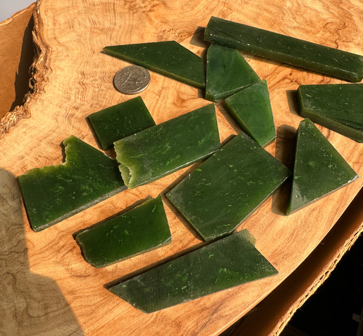 Several dark green rectangular and triangular pieces of natural jade out on a wooden slab, with a coin nearby for scale.