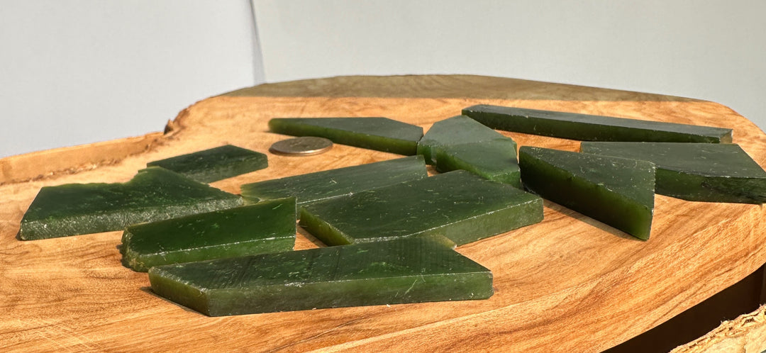 Several dark green rectangular and triangular jade chips arranged on a round wooden slice against a plain light background.