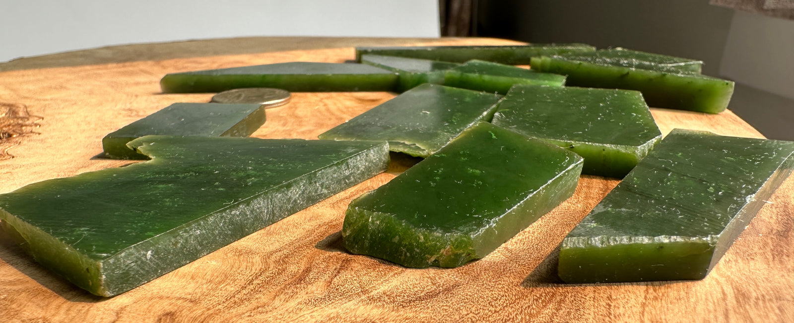 Several translucent green rectangular blocks or slabs arranged on a round wooden slab, with a coin visible for scale.