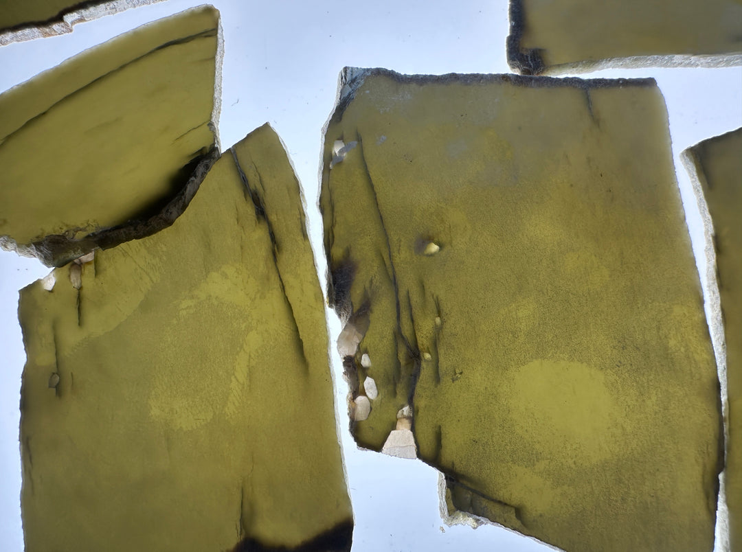 Natural olive-green and yellow-green jade slabs with rough, textured edges and dark charred areas, displayed against a light background.