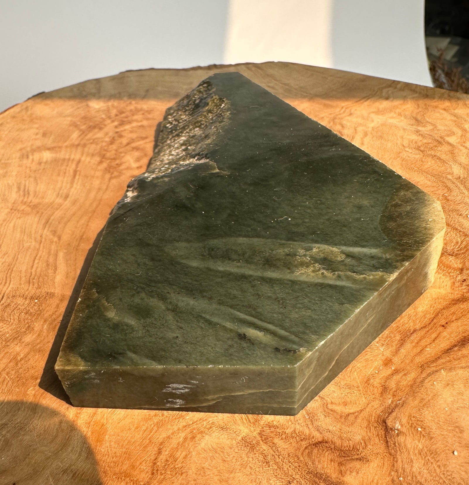 A dark green  jade geometric block displayed on a round wooden surface with warm natural light.