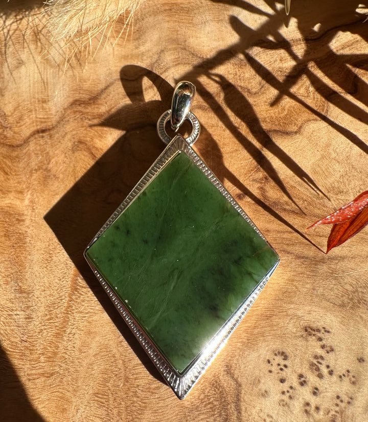 Green jade pendant in a square diamond shape with a textured silver bezel and circular bail