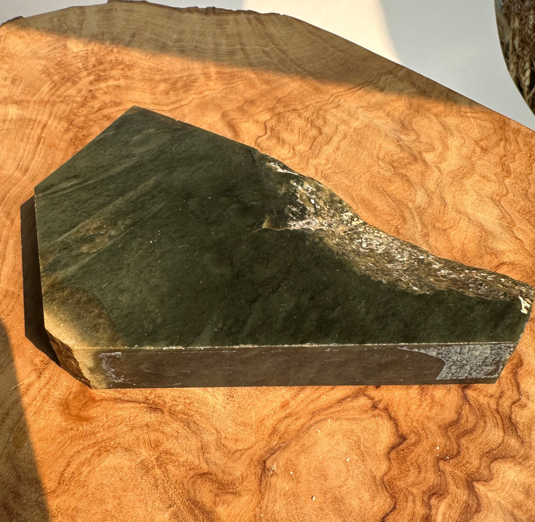 A dark green stone slab with natural wavy veining, displayed on a richly grained wooden surface.