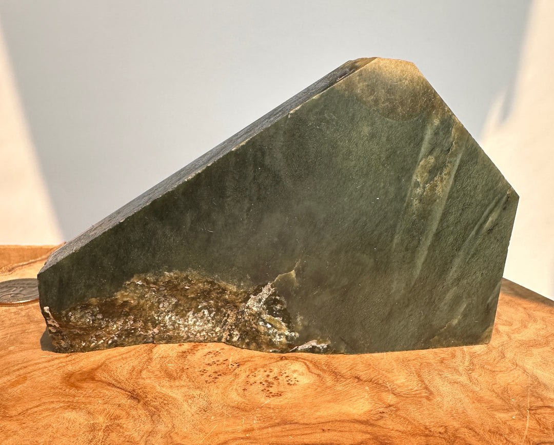 A dark green stone sculpture with a geometric, wedge-like shape, resting on a polished wooden surface against a neutral light gray background.