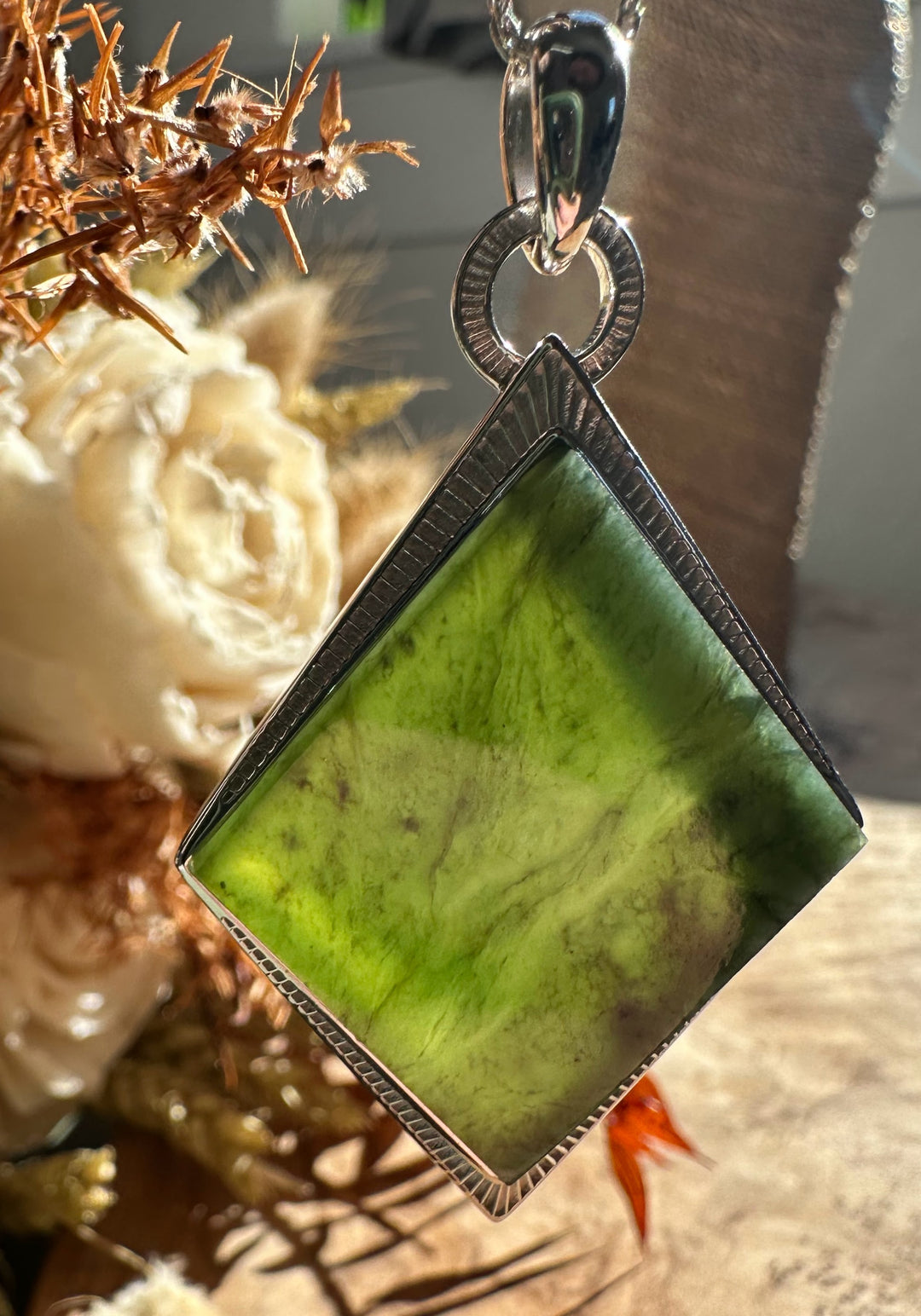 Diamond-shaped green jade pendant in a textured silver bezel with a round bail.
