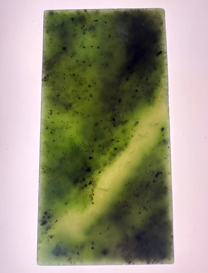 A rectangular translucent green jade with dark speckles and a lighter yellow-green band running diagonally, shown against a plain light background.