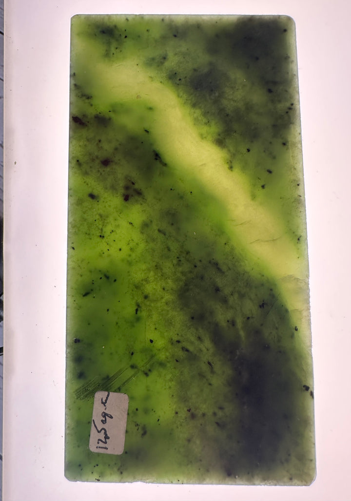 A rectangular green jade slab with natural marbling, dark veining, and a small handwritten price tag near the bottom left, photographed against a white background.