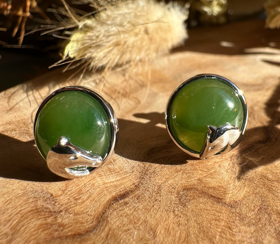 Pair of round green jade stud earrings with silver horse head accents on a wooden surface