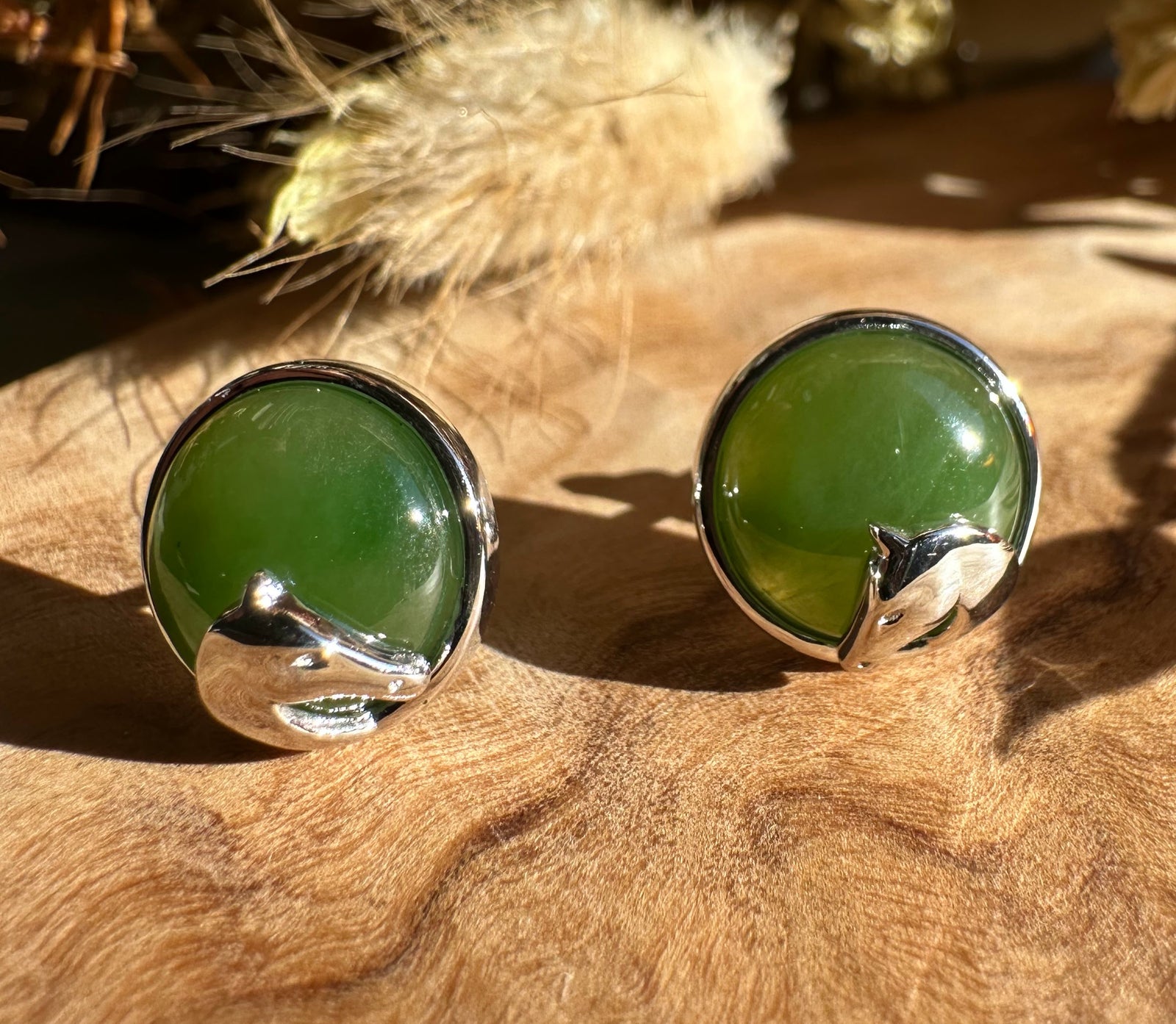 Pair of round green jade stud earrings with silver horse head accents on a wooden surface