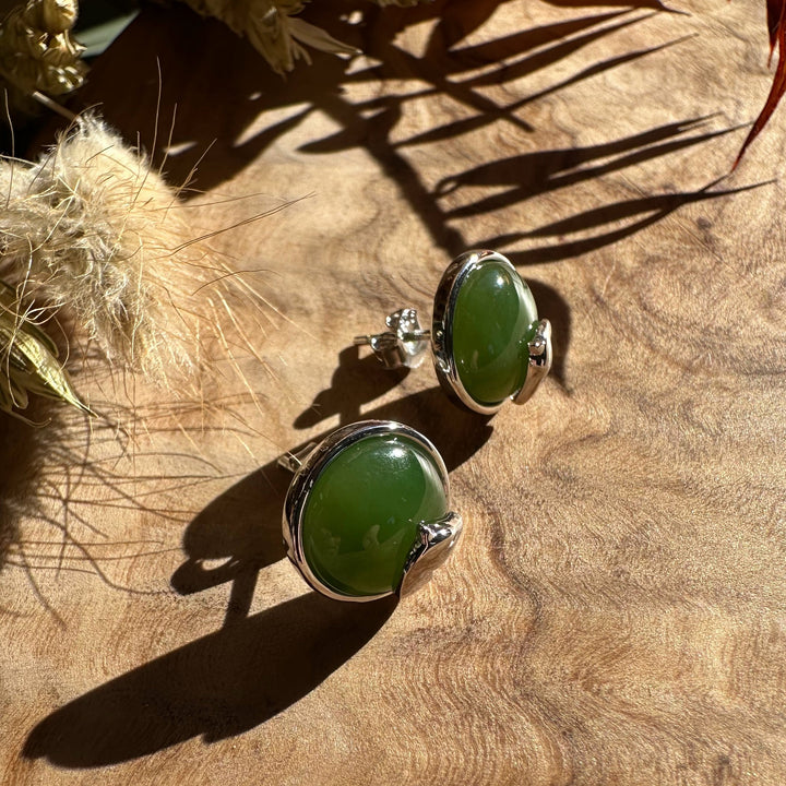Two round green jade stud earrings with silver horse head accents resting on a wooden surface