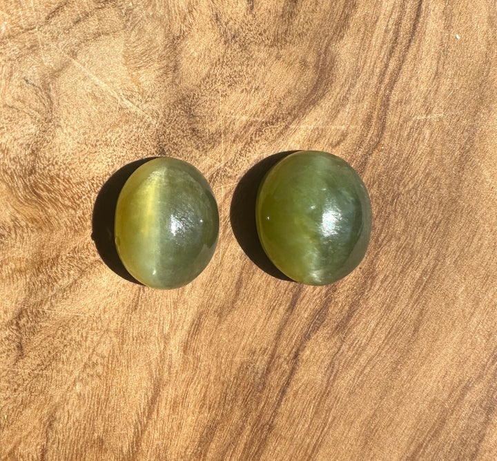 Pair of 12x10mm Siberian Cats Eye Cabochons on a wooden surface