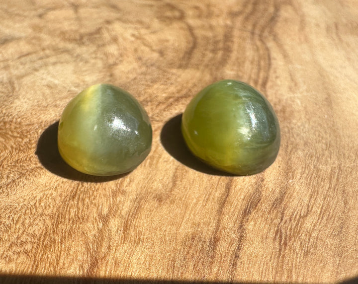 Two green Siberian Cats Eye Cabochons resting on wood
