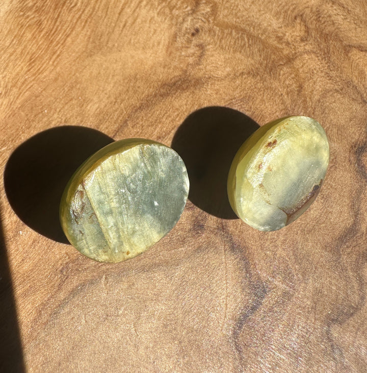 Two oval green Siberian Cats Eye cabochons partially visible on a wood surface