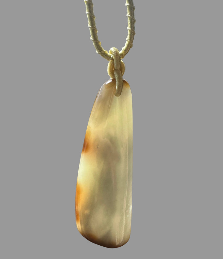 Close-up of pale nephrite jade pendant tied with a wrapped yellow cord knot against a gray backdrop