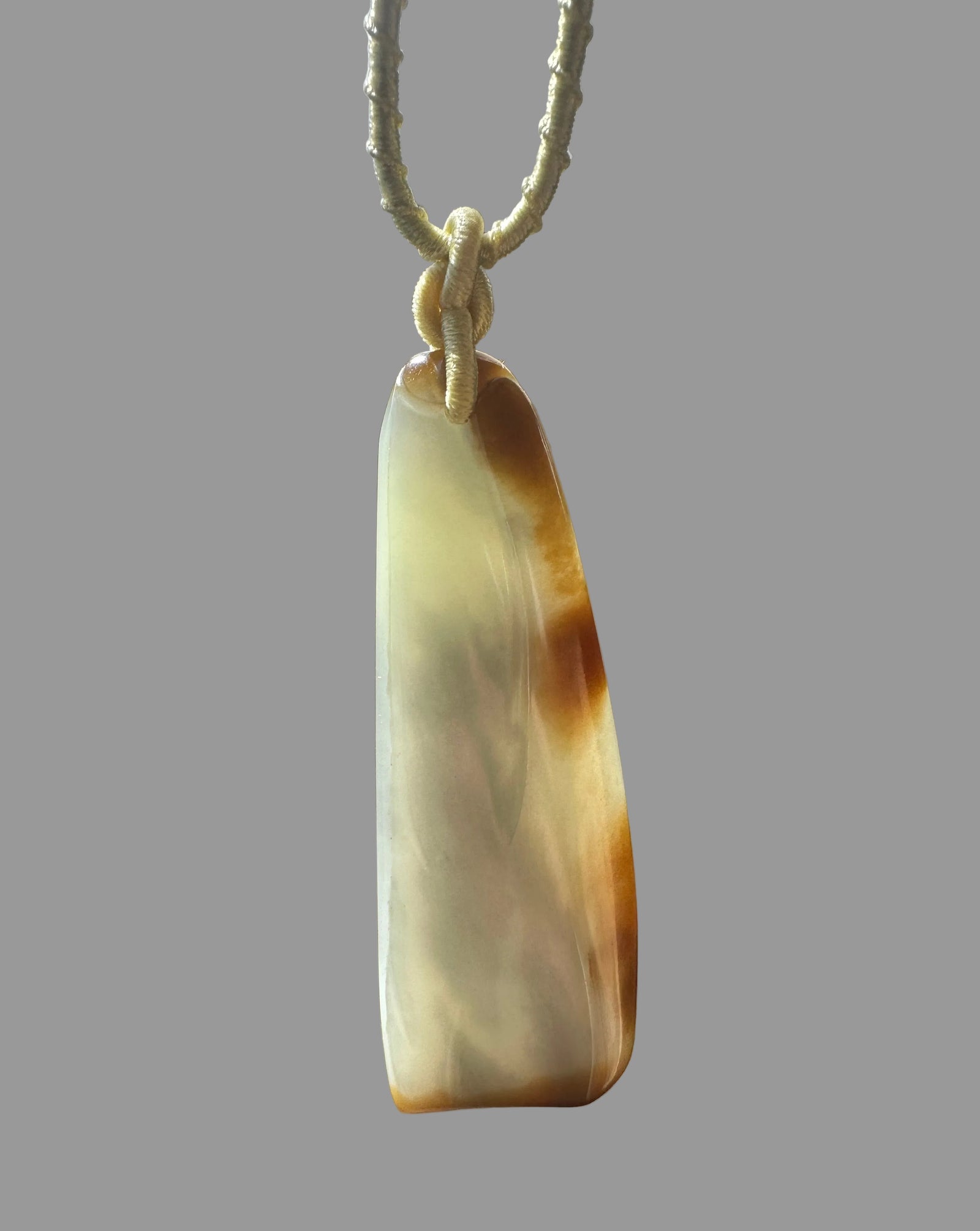 65mm nephrite Loulan jade pendant in pale cream with a knotted beige cord against a wood background