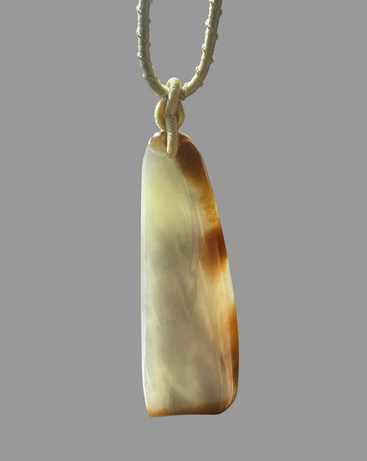 65mm nephrite Loulan jade pendant in pale cream with a knotted beige cord against a wood background