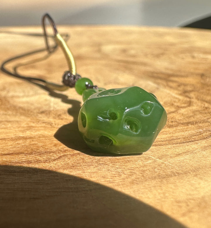 Close-up of the green carved pendant with holes on a black cord