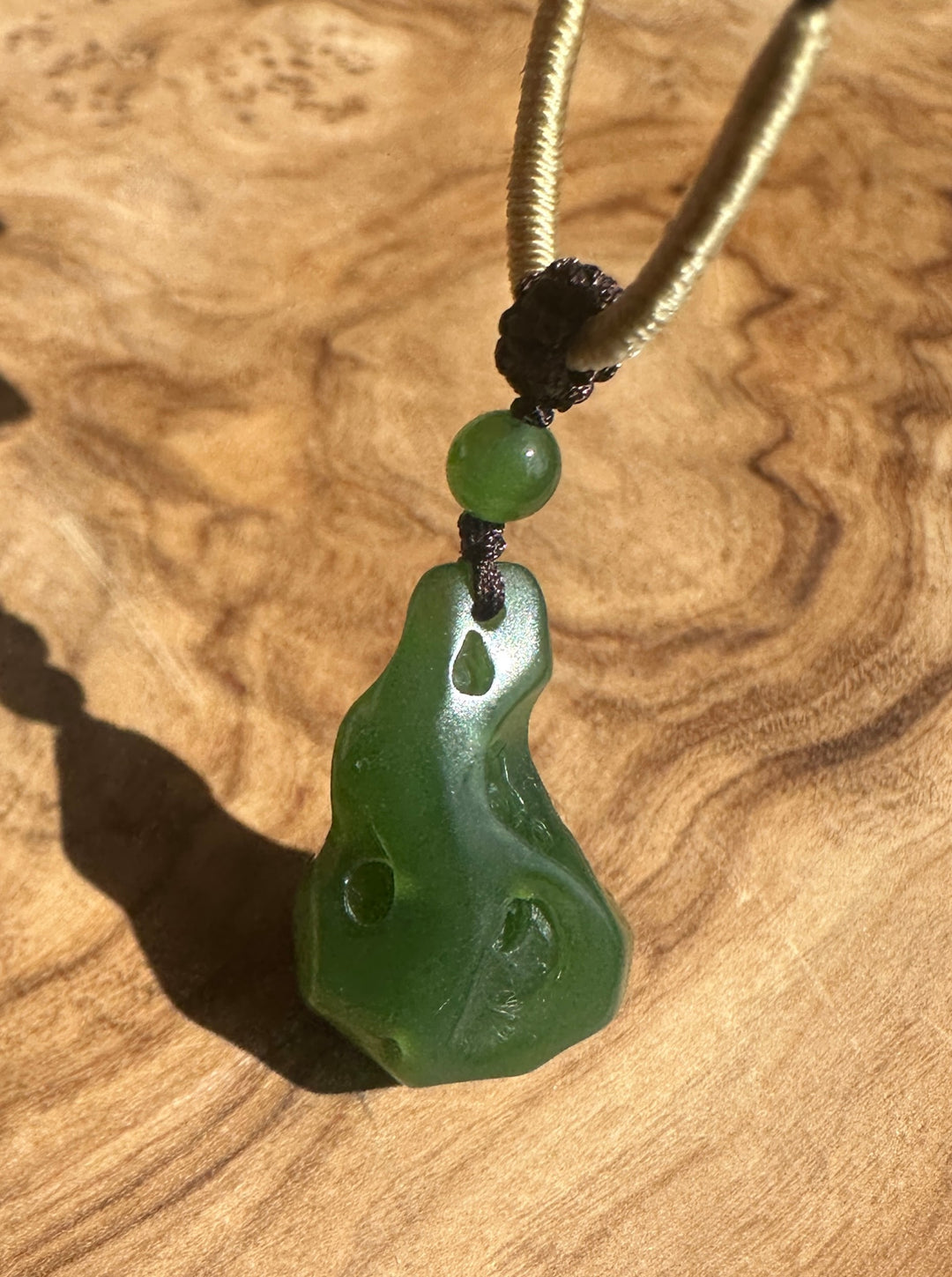 Close up of a rich green abstract pendant on a beige cord with a dark knot