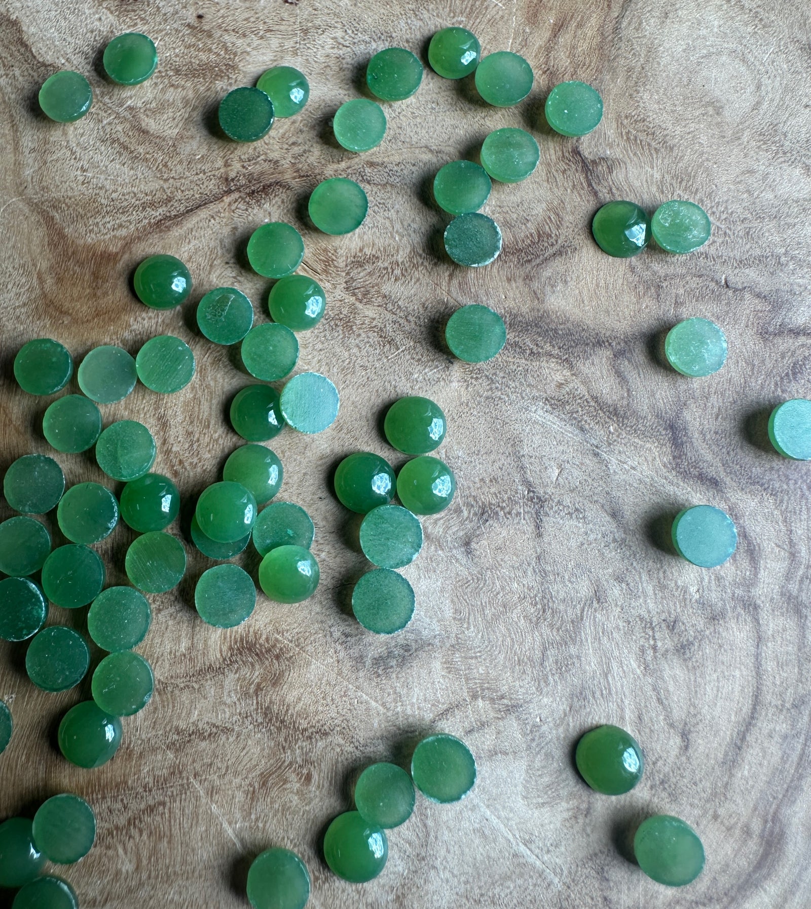 Several light green 5mm Canadian jade round cabochons spread across a wood surface