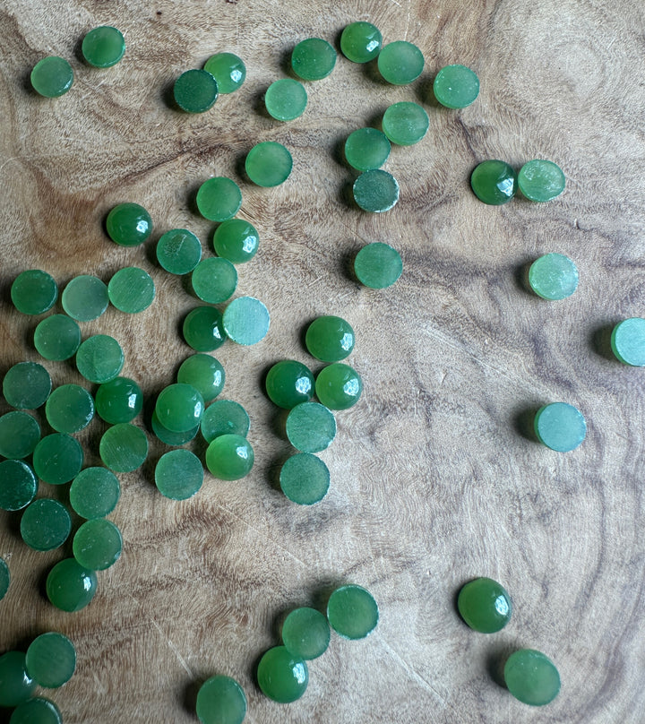Several light green 5mm Canadian jade round cabochons spread across a wood surface