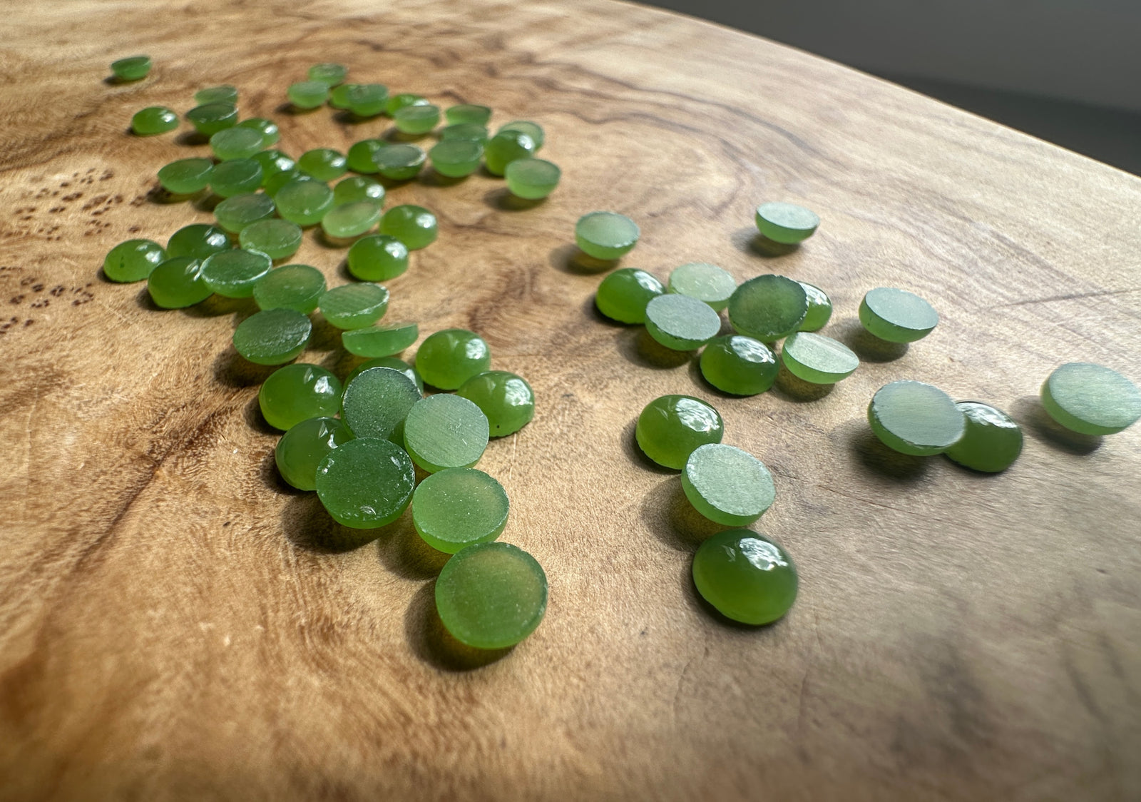 Group of light green 5mm Canadian jade round cabochons scattered on wood