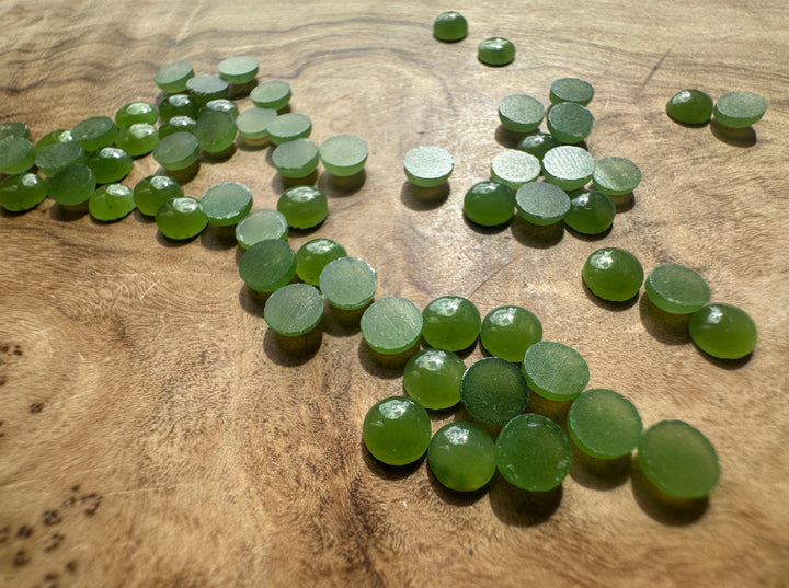 Vintage light green Canadian jade round cabochons on a wood surface with matte backs visible