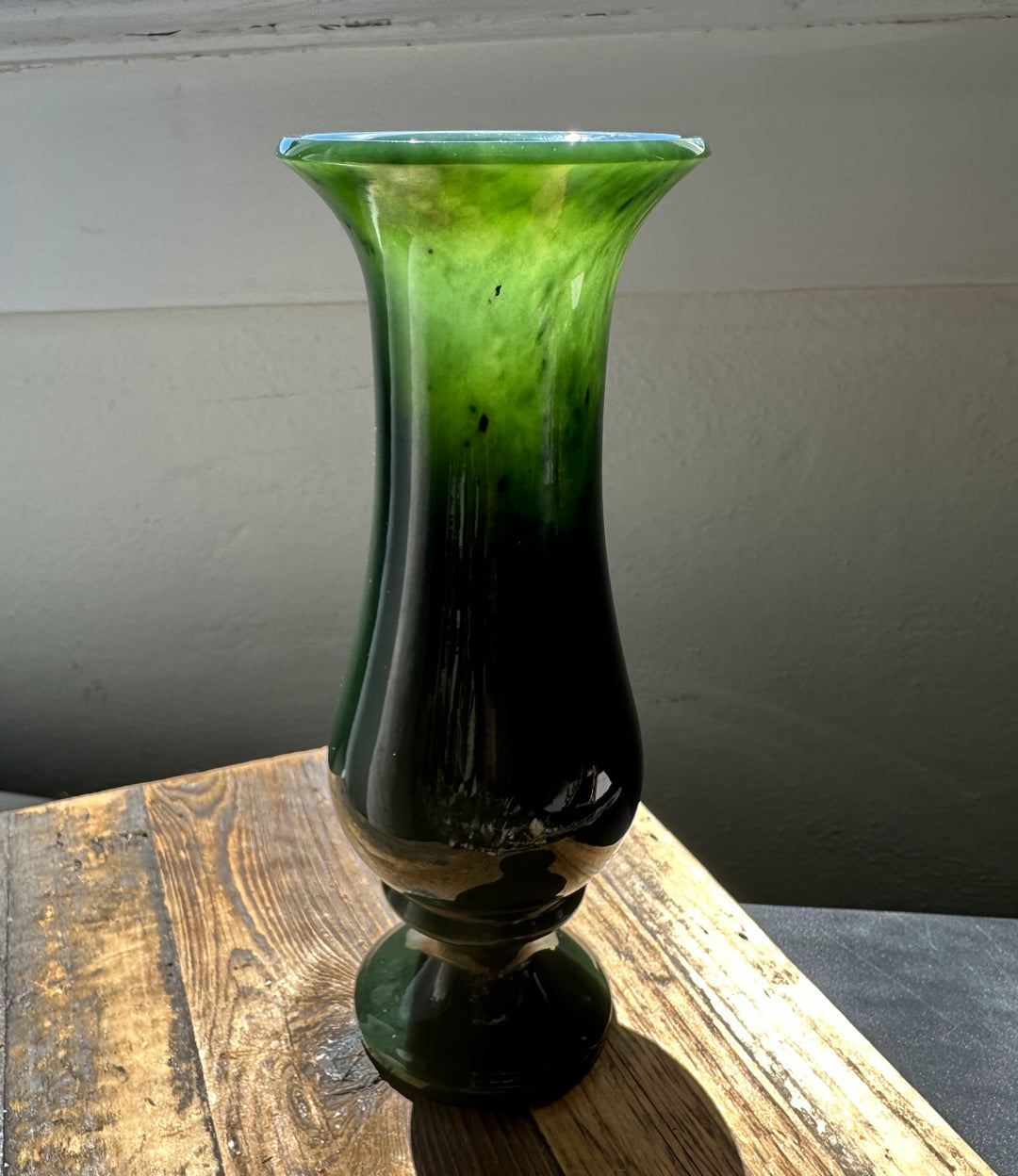 Tall emerald green glass vase with a flared rim sitting on a rustic wooden table.