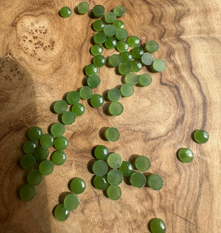 Vintage light green Canadian jade round cabochons scattered on a wooden surface