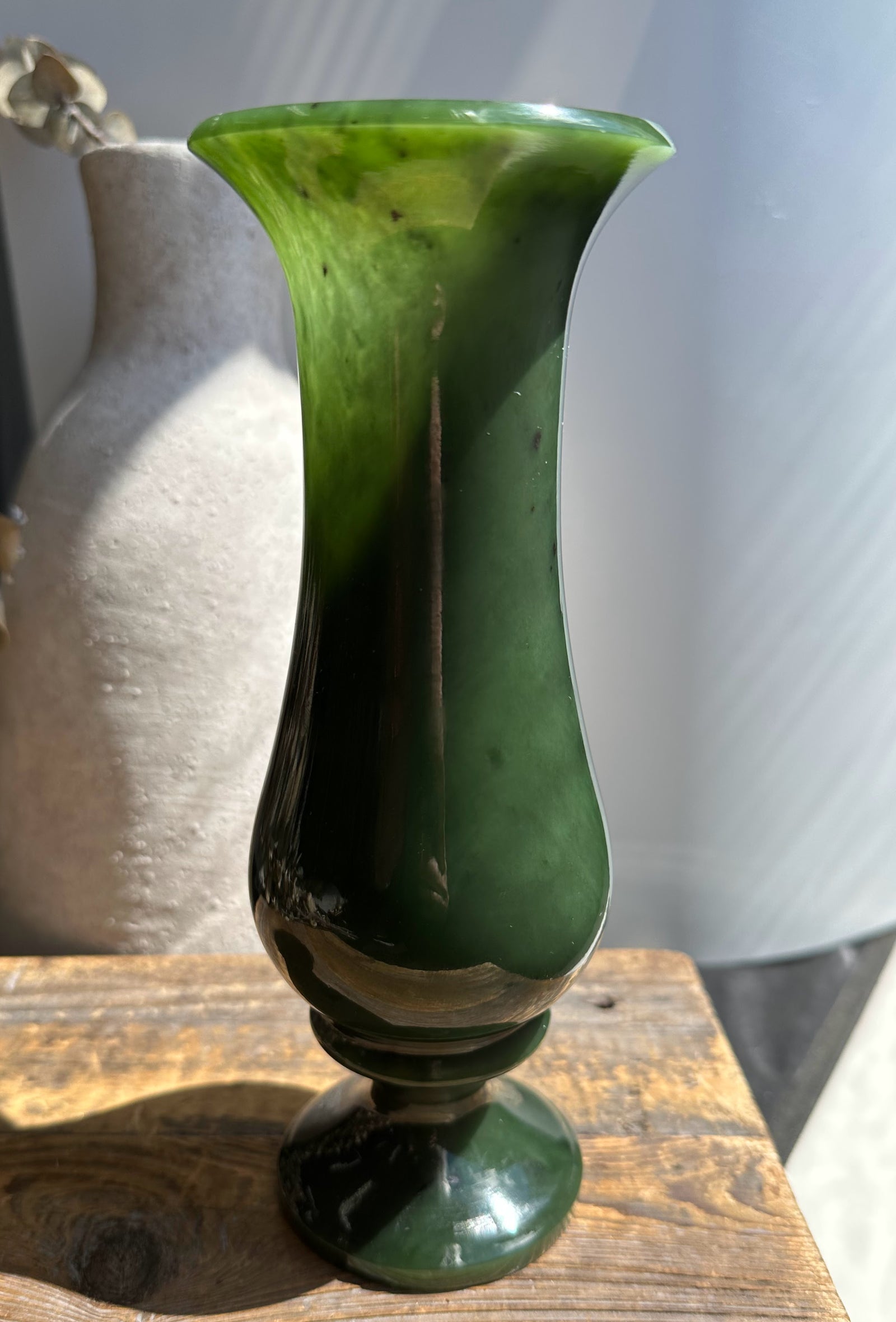 Close up of emerald glass vase with a wide flared rim and narrow neck.
