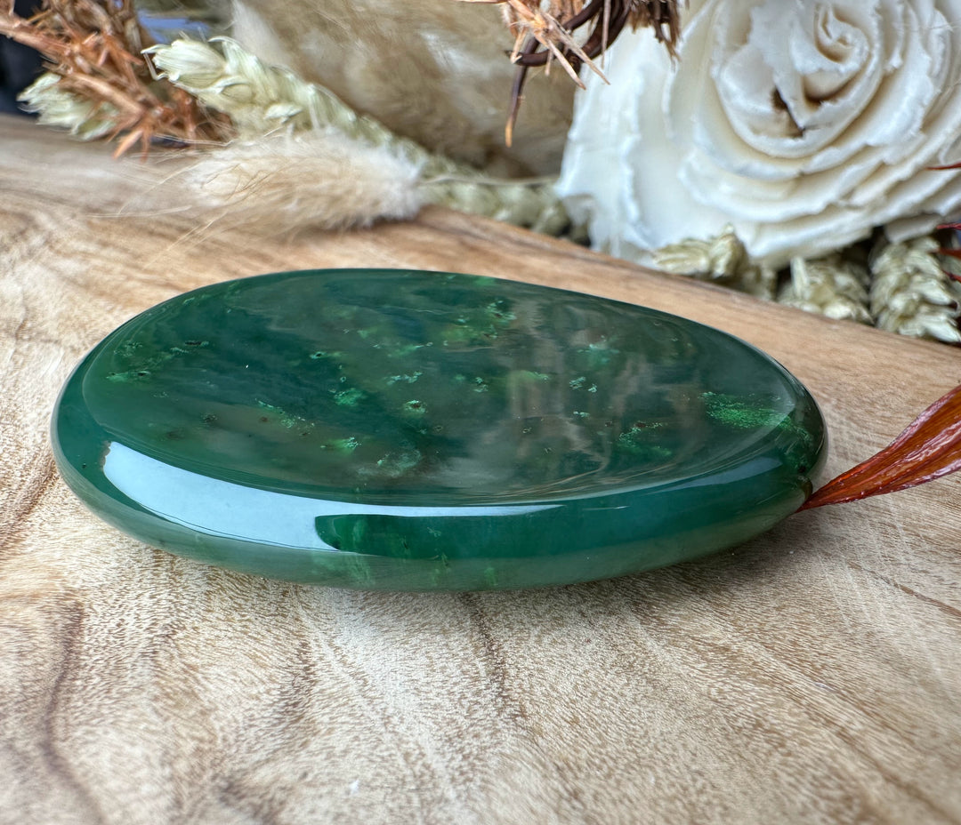 Green jade worry stone with a reddish brown cord attached resting on a wooden surface