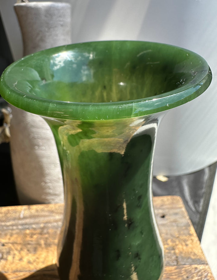 Glossy jade green vase with curved silhouette and darker base on a wooden surface.