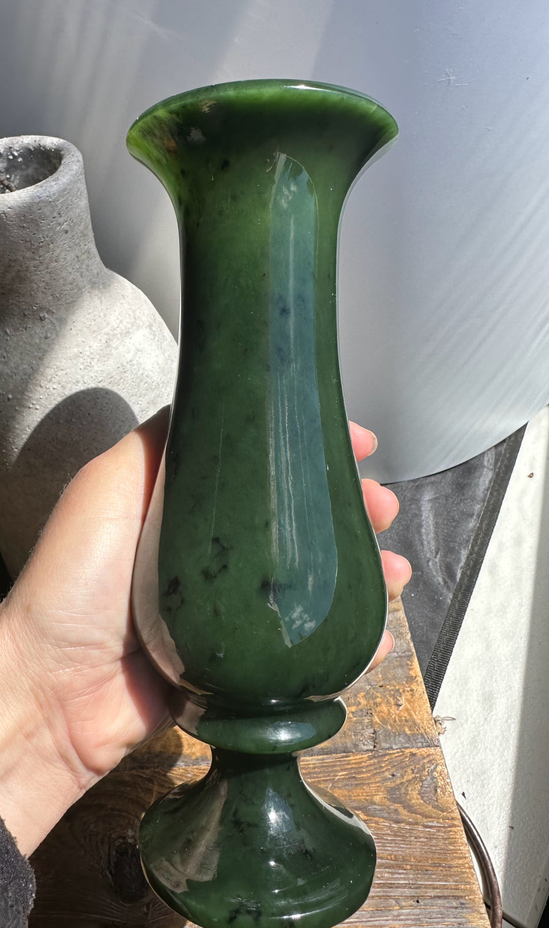Tall jade green vase with a flared trumpet-shaped rim held in a hand.
