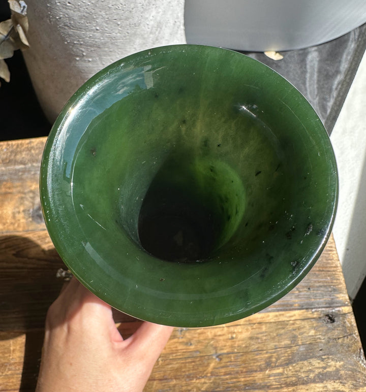 Top-down view into a glossy emerald green Siberian Jade Vase held over a wooden surface.
