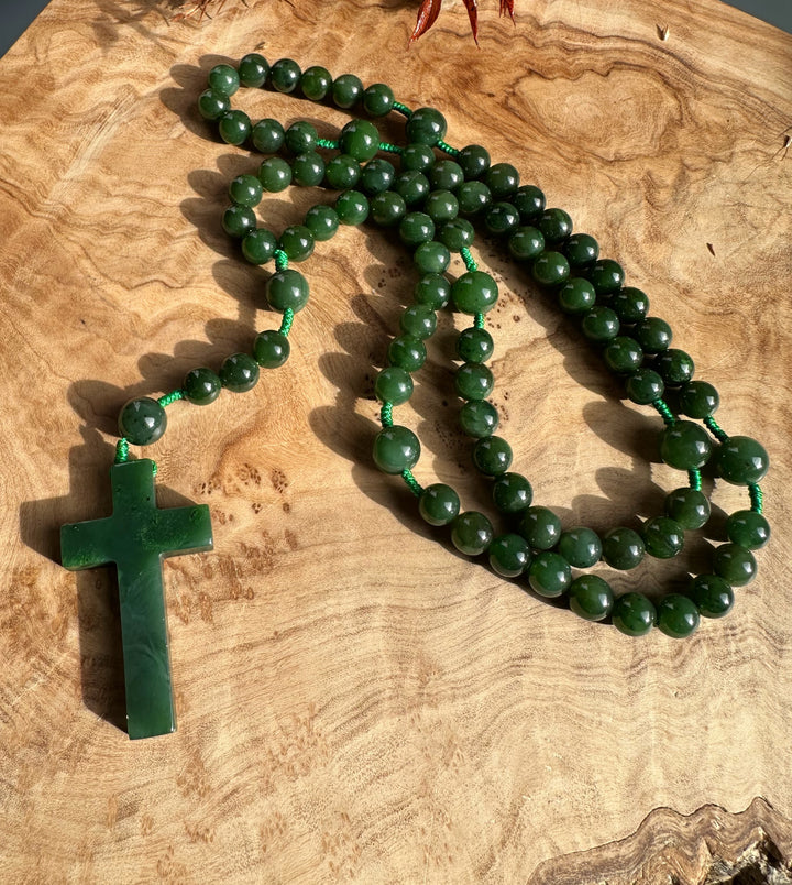 Dark green jade rosary beads with a large jade cross pendant laid on a wooden surface.