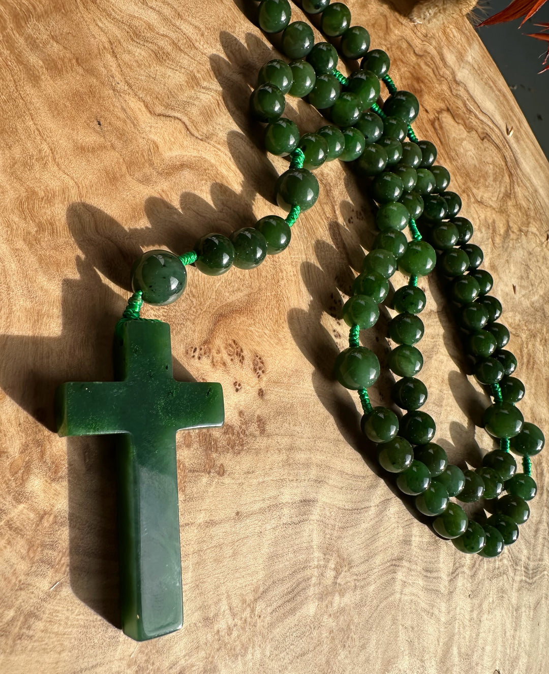 Close up of green jade rosary beads draped around a jade cross pendant on a wooden surface.