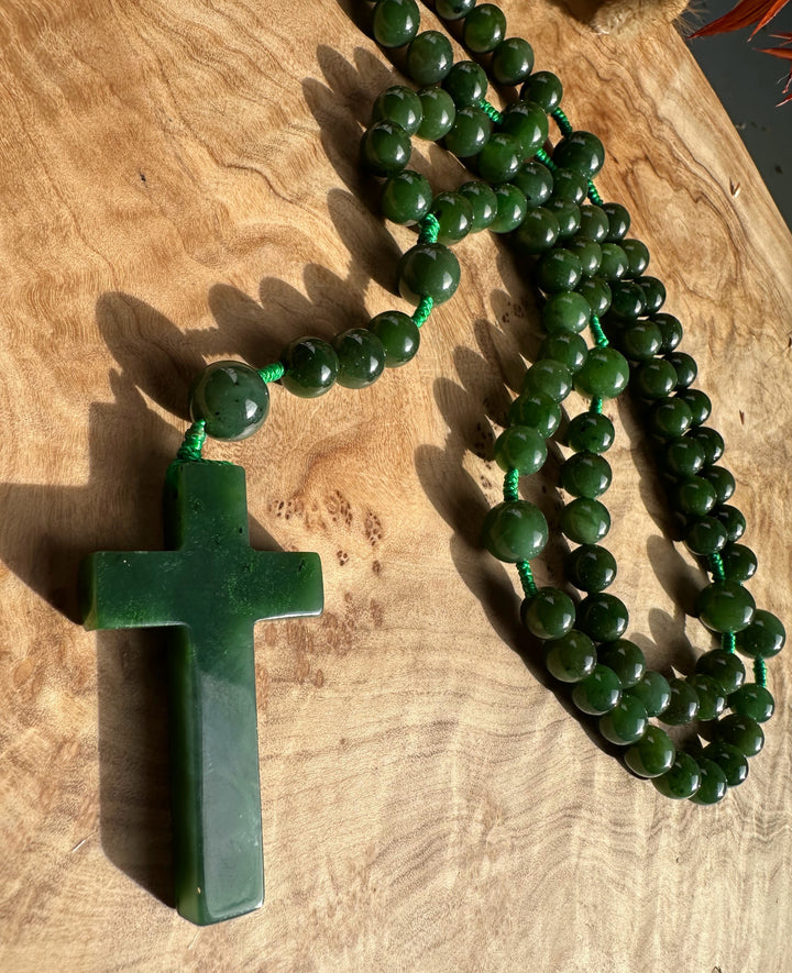 Close up of green jade rosary beads draped around a jade cross pendant on a wooden surface.