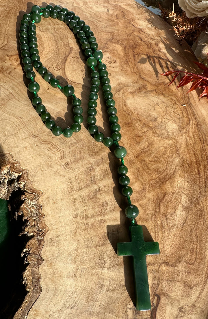 Jade rosary beads spread across a wood surface with a cross pendant at the bottom end.