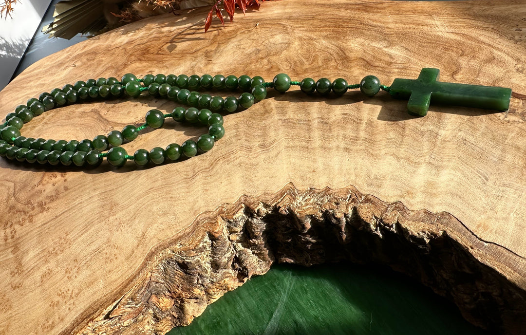 Jade rosary beads laid out on a wooden tabletop with a green cross at the end.