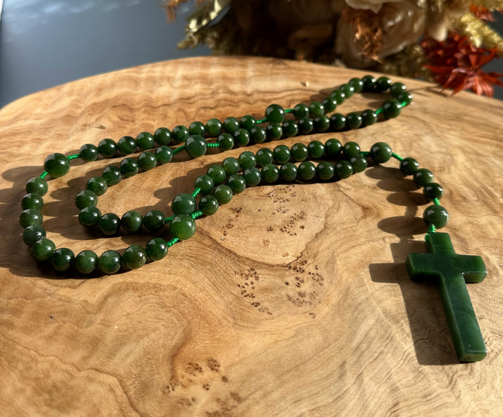 Jade rosary beads with a green cross pendant resting on a wooden surface.