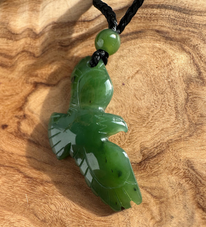 Close-up of jade eagle pendant carved from green jade with a round green bead on a black cord