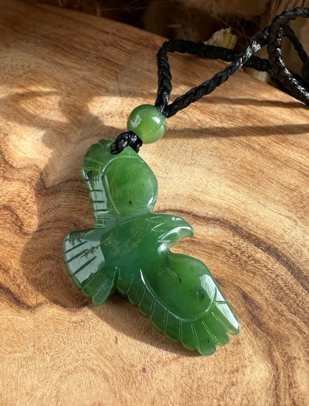 Green jade eagle pendant on a black braided cord with a round bead