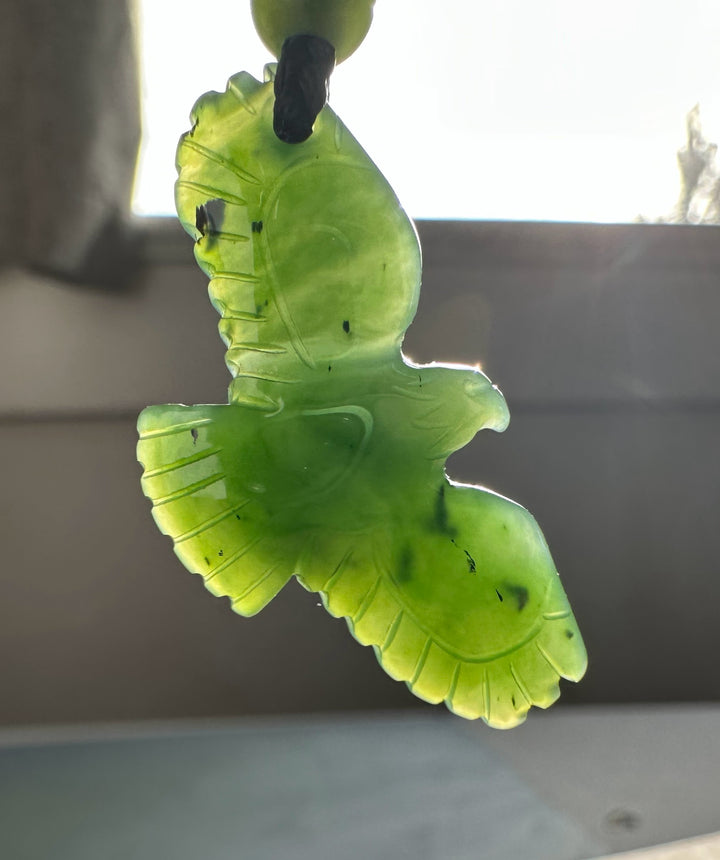 Jade eagle pendant suspended from a black cord with translucent green carving and feather details.