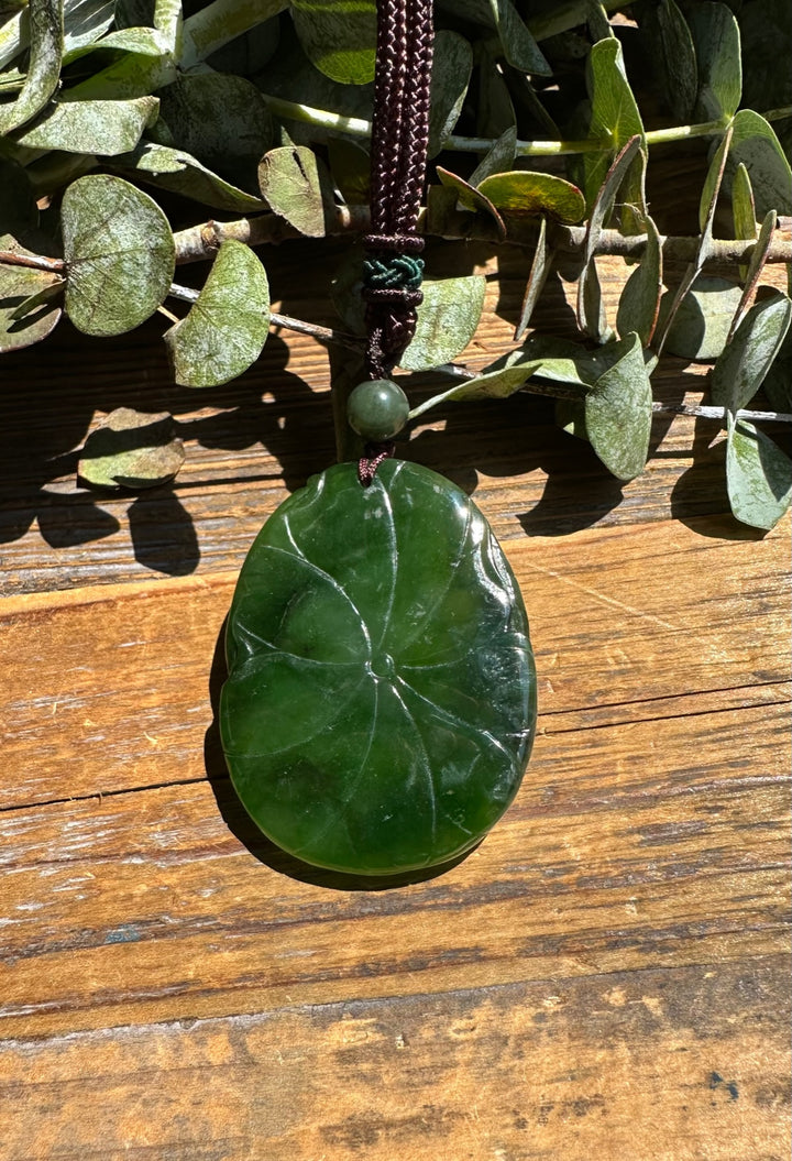 Deep green round jade pendant with natural swirl patterns hanging from a brown cord with a green bead