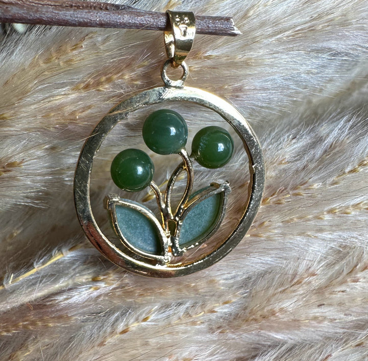 Circular gold pendant featuring a jade flower with three green bead blossoms and two jade leaves.