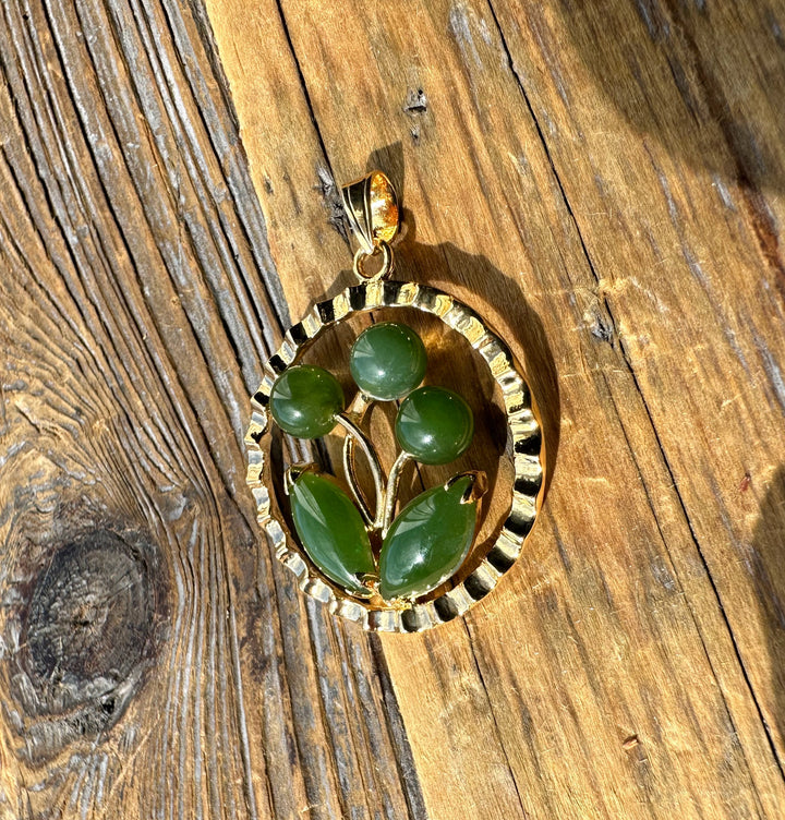 Jade flower pendant with circular gold frame and leaf and bead accents on wood surface