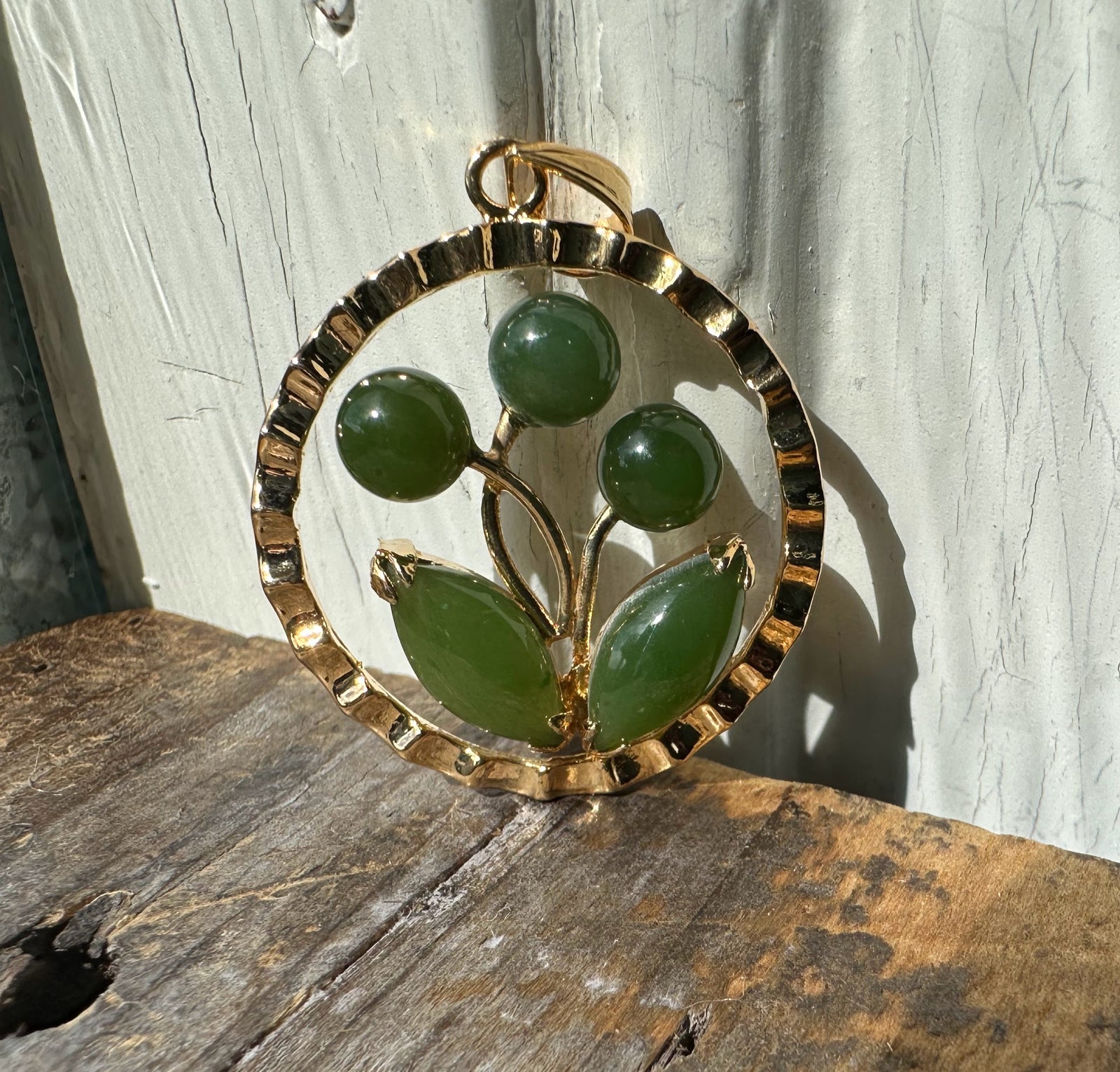 Gold circular pendant with a jade flower motif featuring three buds and two leaves