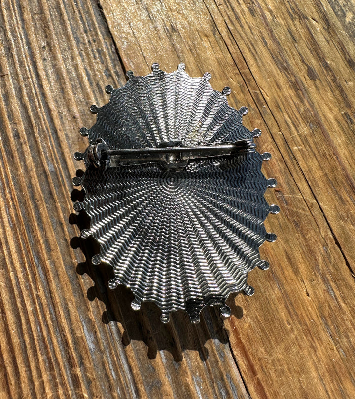Radial textured back of oval brooch with pin mechanism shown on wood surface.