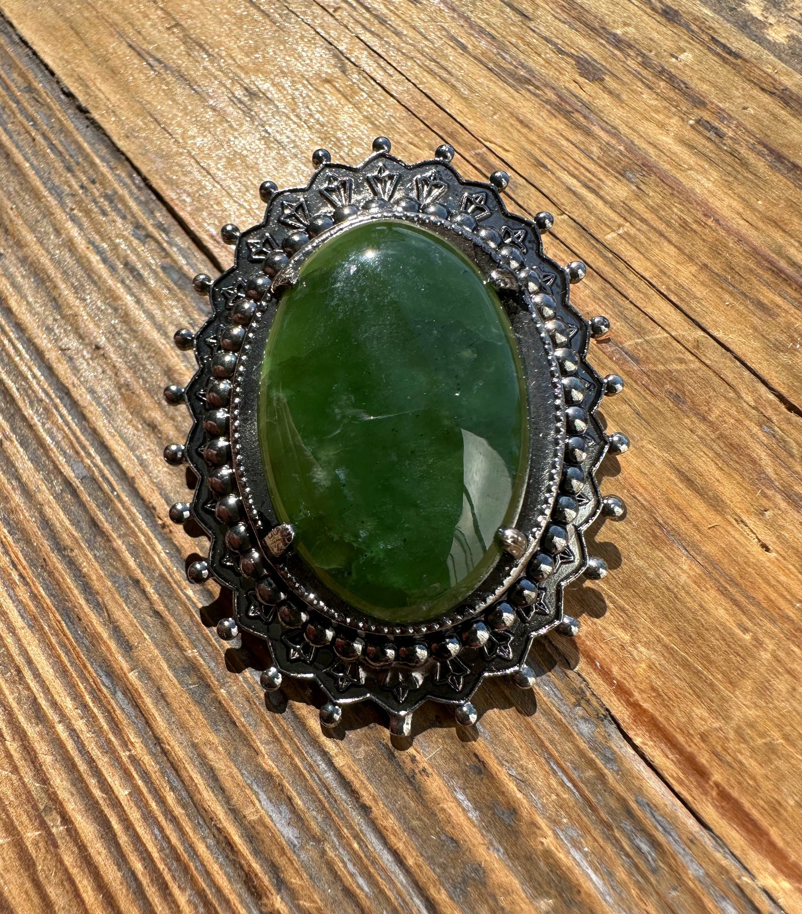 Close-up of vintage jade oval brooch showing a green jade centerpiece in a dark metal scalloped frame with bead detailing.