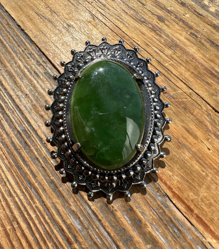 Close-up of vintage jade oval brooch showing a green jade centerpiece in a dark metal scalloped frame with bead detailing.