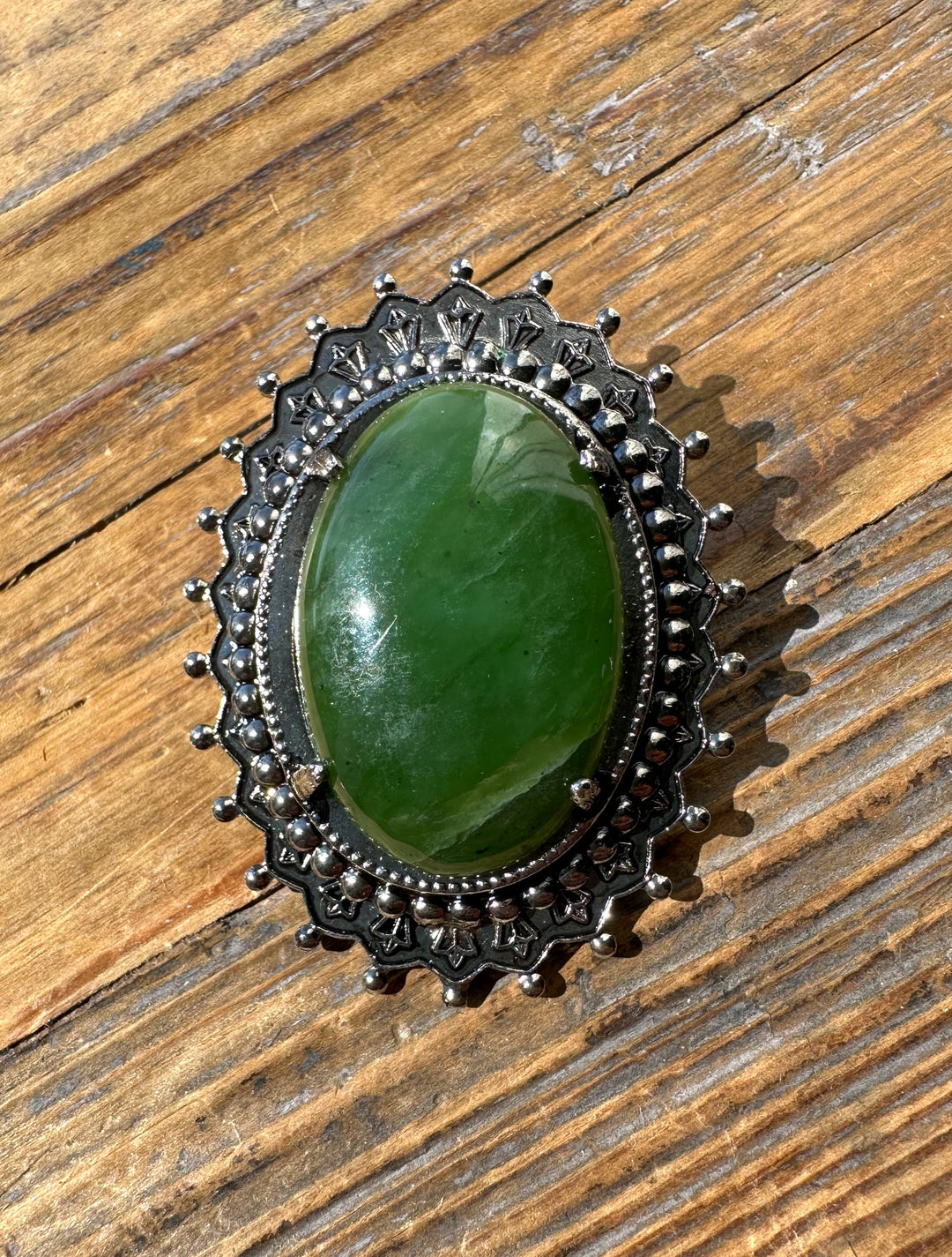 Vintage jade oval brooch with a green central stone framed by ornate silver filigree and a beaded border.